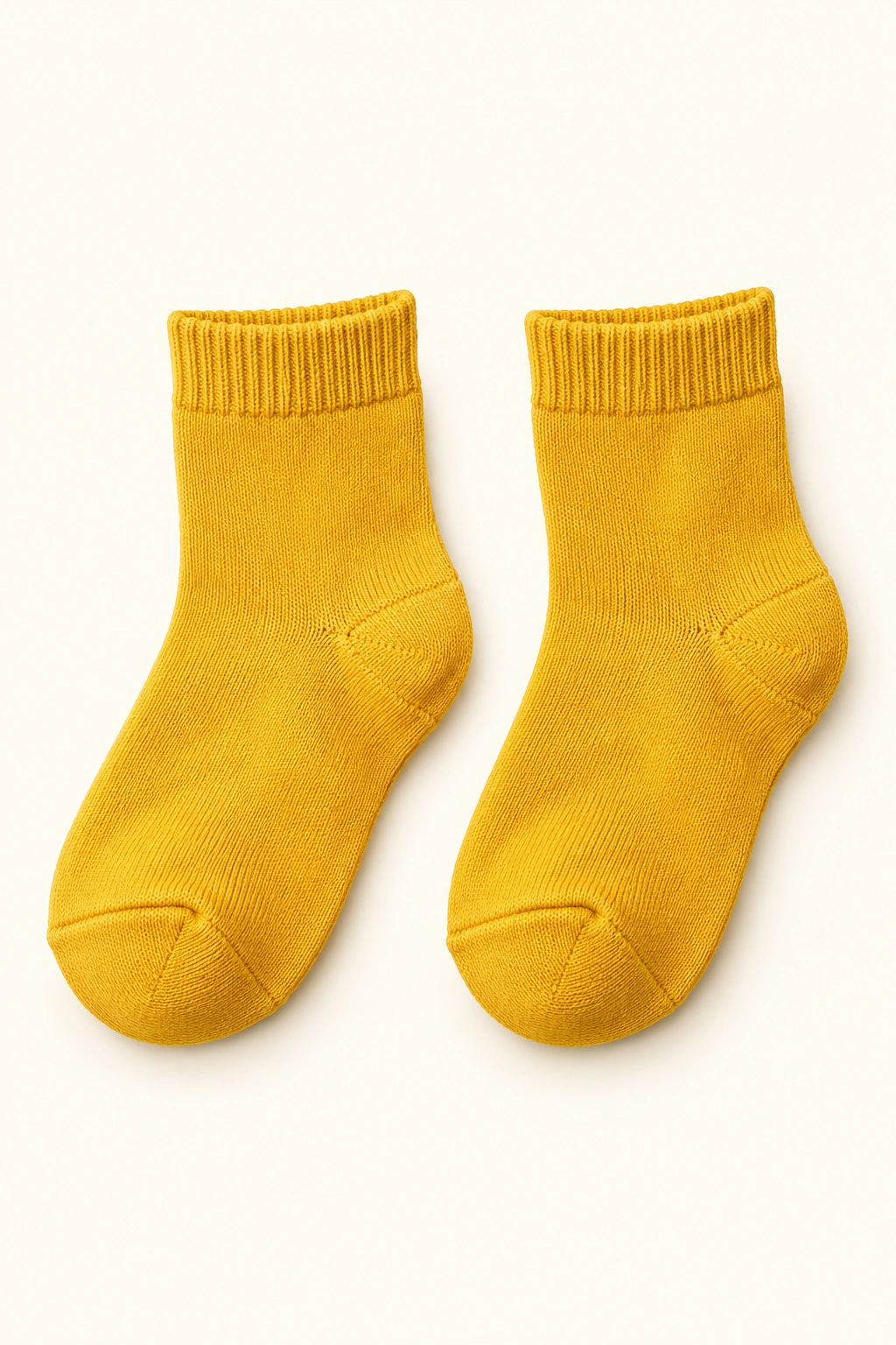 Ein Paar senfgelbe Kinder-Socken liegt vollständig und getrennt sichtbar vor hellem Hintergrund.