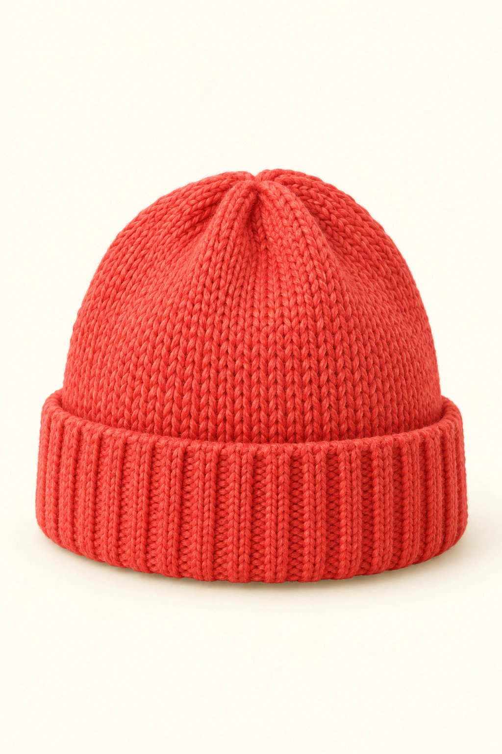 Eine korallrote gestrickte Kinder-Mütze mit breitem Umschlag steht vollständig sichtbar vor hellem Hintergrund.
